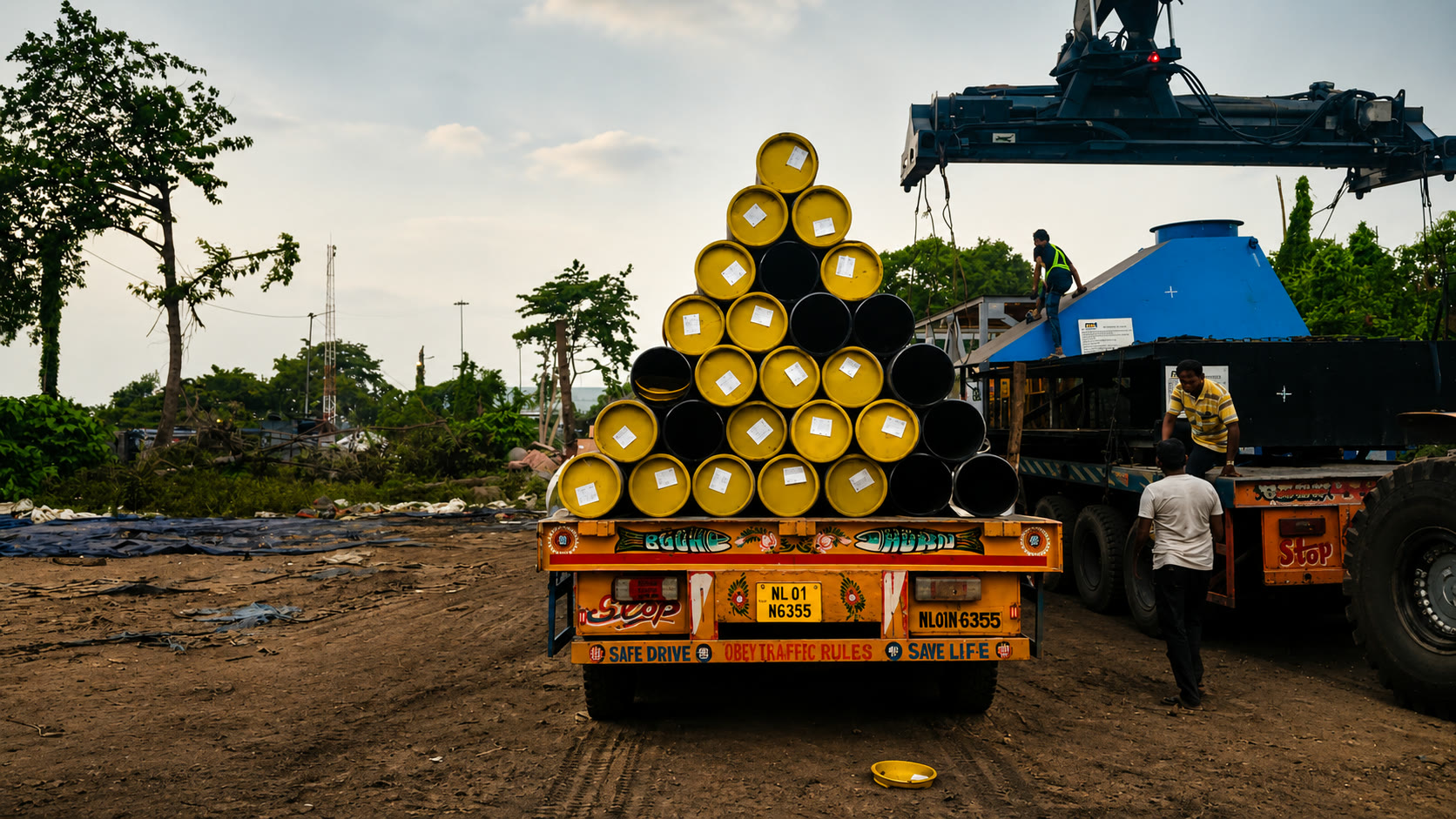 Workers and machinery handling a load of yellow-ended pipes